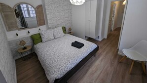 A bedroom with a bed, a wardrobe, a chair, a lamp, and a mirror. - En Hypercentre, au Calme, Avec Cour Privative Aménagée, Appartement Rénové (Arras)