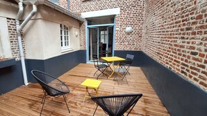 A patio with wooden flooring, a yellow table, and two black chairs. - En Hypercentre, au Calme, Avec Cour Privative Aménagée, Appartement Rénové (Arras)