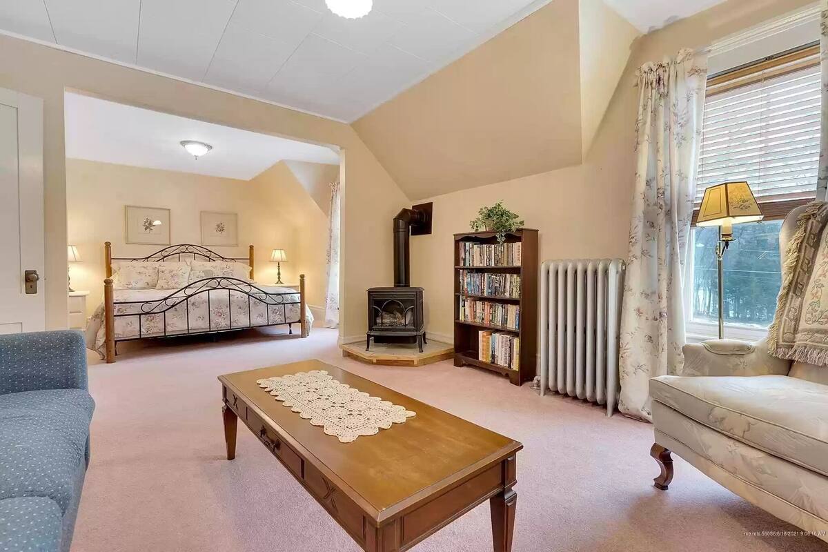 Ein gemütliches Zimmer mit einem Bett, einem Sofa, einem Tisch, einem Bücherregal, einem Heizkörper und einem Fenster mit Vorhängen.
