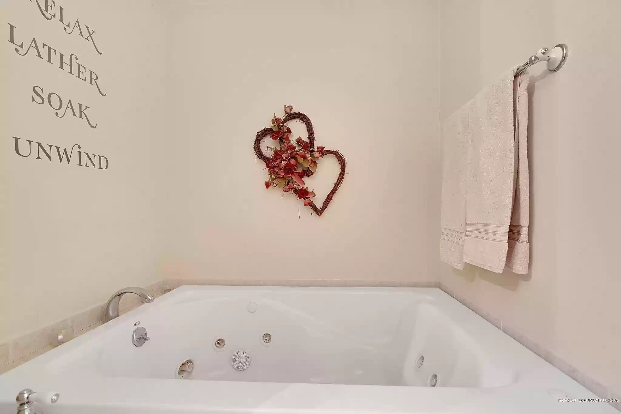 Un baño con una bañera blanca, una decoración con forma de corazón en la pared y un perchero con una toalla doblada.