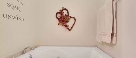 Un baño con una bañera blanca, una decoración con forma de corazón en la pared y un perchero con una toalla doblada.