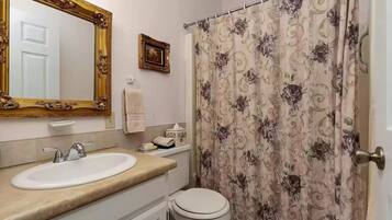 A bathroom with a white sink, a toilet, a shower curtain with a floral pattern, and a mirror with an ornate frame.