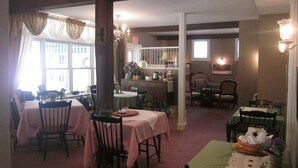 Un comedor con varias mesas y sillas, una cocina al fondo y vistas al exterior a través de amplios ventanales.