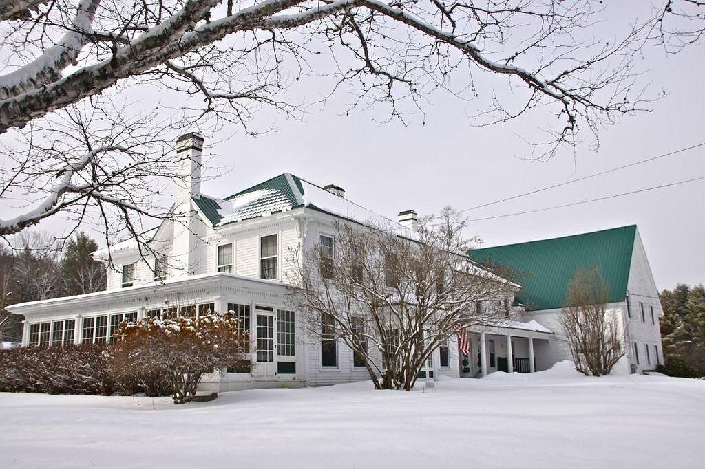 Una casa grande y blanca de dos pisos con techo verde, rodeada de nieve.