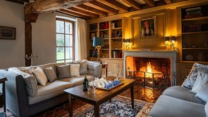 A cozy living room with a fireplace, a sofa, a coffee table with chess pieces, and a bookshelf.