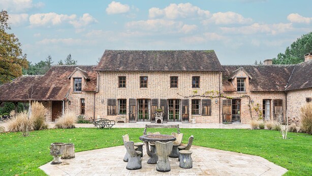 A large brick building with a central courtyard, featuring a stone table and chairs, surrounded by a well-maintained lawn.