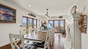 A dining area with a wooden table and white chairs, large windows, and a view of the outdoors. - Mountainside Chateau spectacular views and sunsets. 15 min to downtown Ashland! (Ashland)