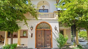 A building with a wooden double door, a balcony with a railing, and a small garden area with trees and a stone pathway. - Mountainside Chateau spectacular views and sunsets. 15 min to downtown Ashland! (Ashland)