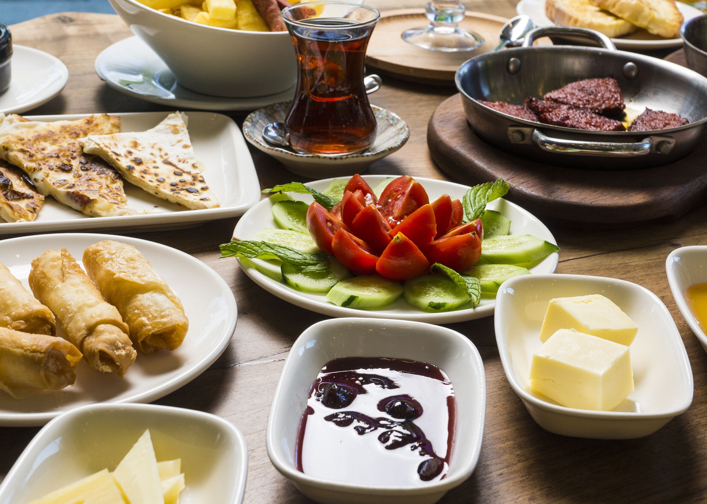 A table with various dishes including flatbreads, a salad with tomatoes and cucumbers, and bowls of butter and a dark sauce.