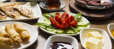 A table with various dishes including flatbreads, a salad with tomatoes and cucumbers, and bowls of butter and a dark sauce.