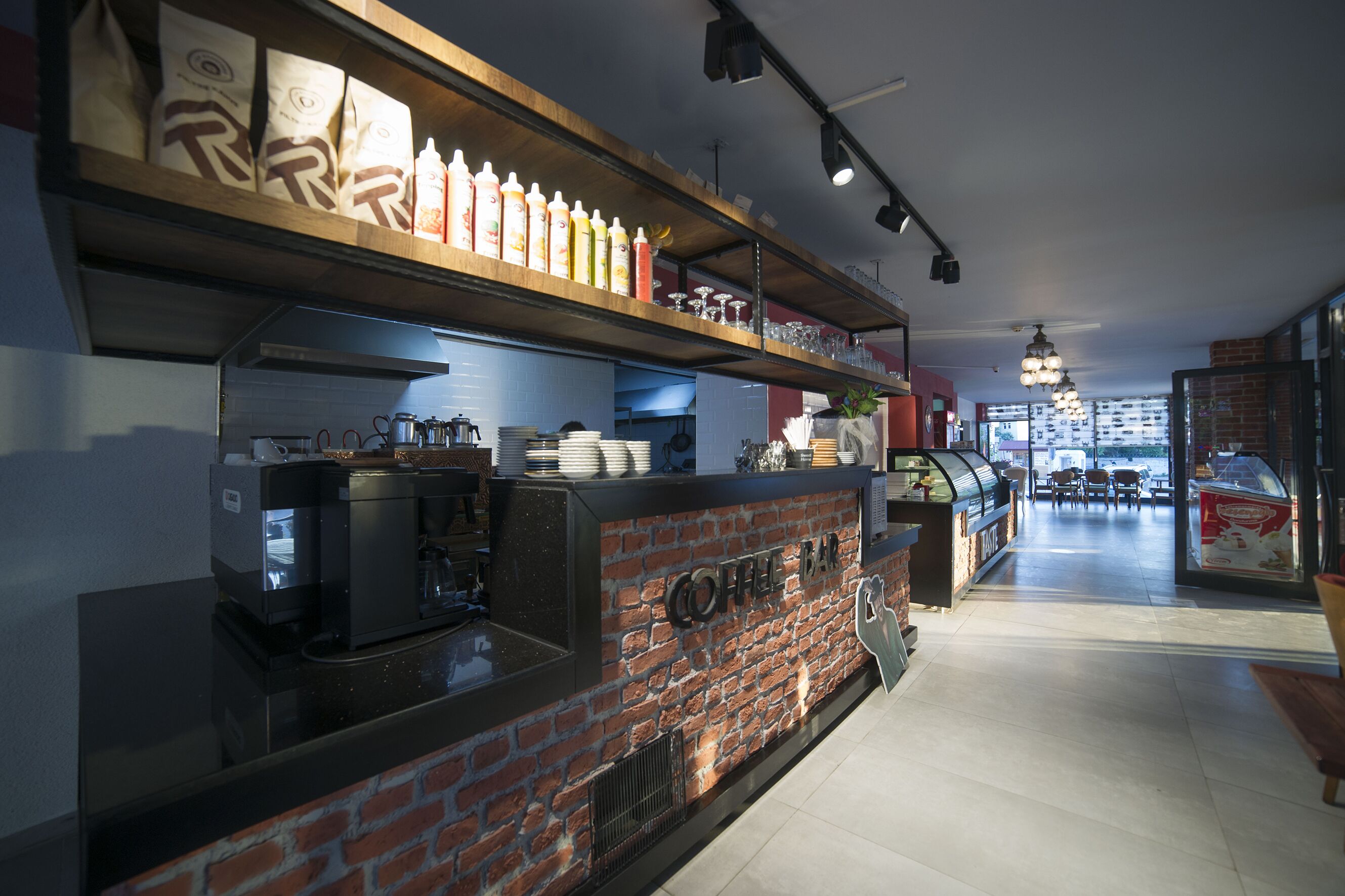 A coffee bar with a brick wall, shelves with coffee bags, and a coffee machine.