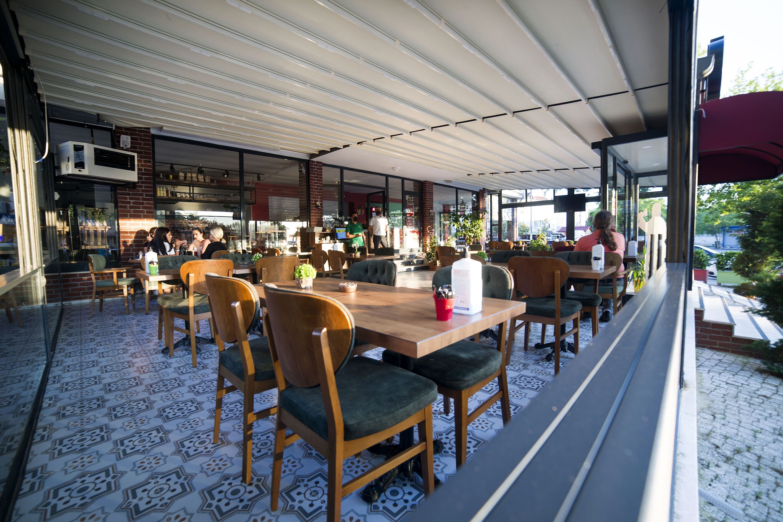 An outdoor dining area with wooden tables and chairs, a patterned floor, and a view of the street.