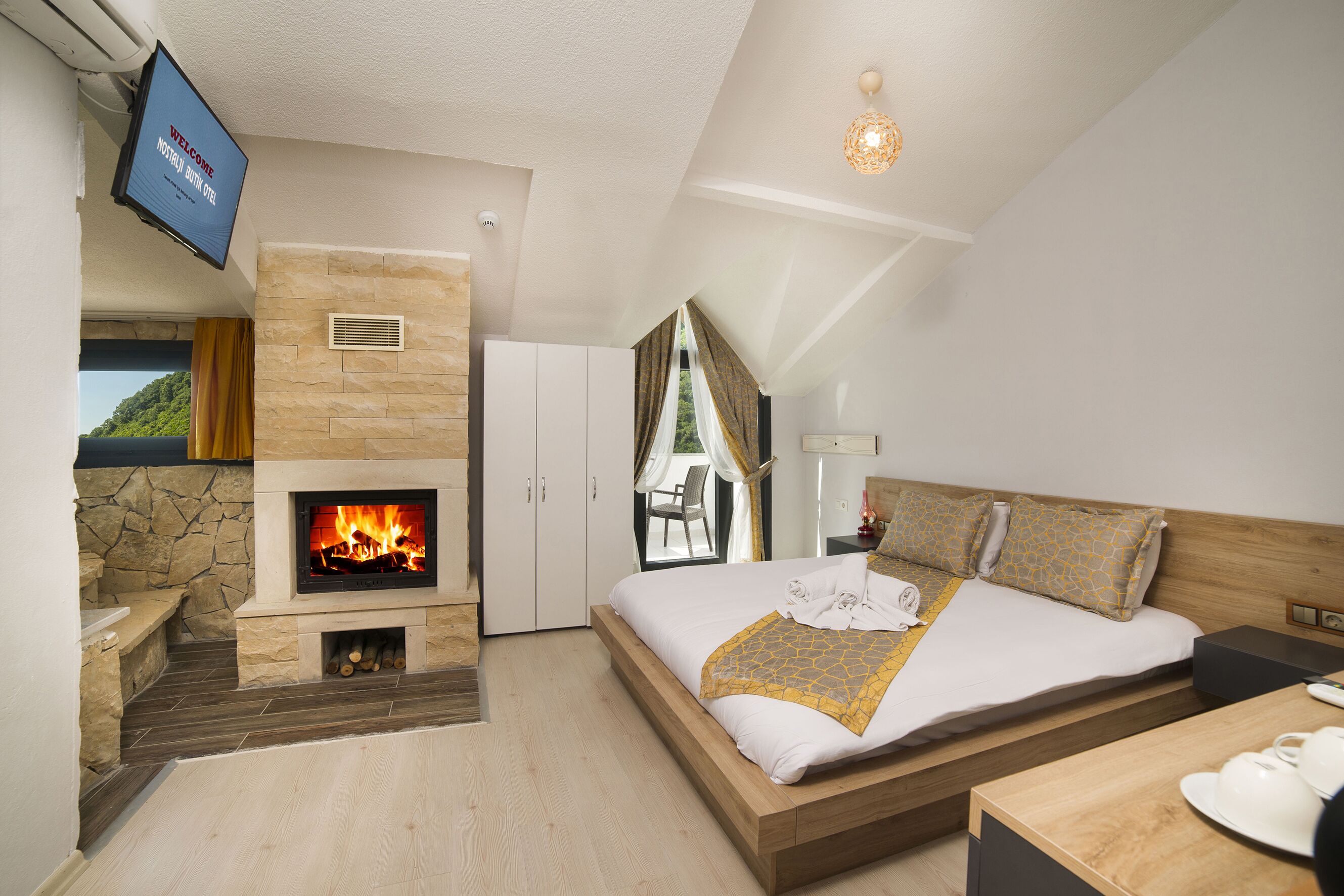 Una habitación de hotel moderna con chimenea, una cama con cabecero de madera, un televisor montado en la pared y vistas al exterior.