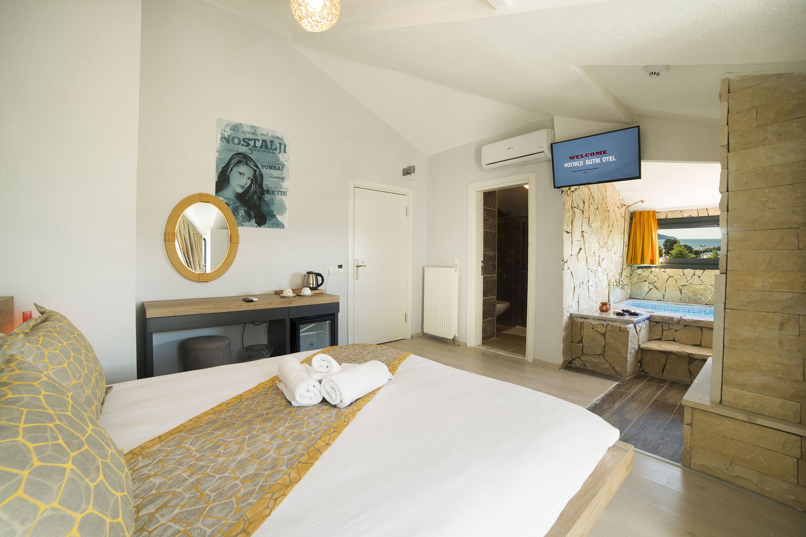 Ein Hotelzimmer mit Bett, Schreibtisch, Spiegel, Fernseher und einem Badezimmer mit Steinwand und Ausblick.