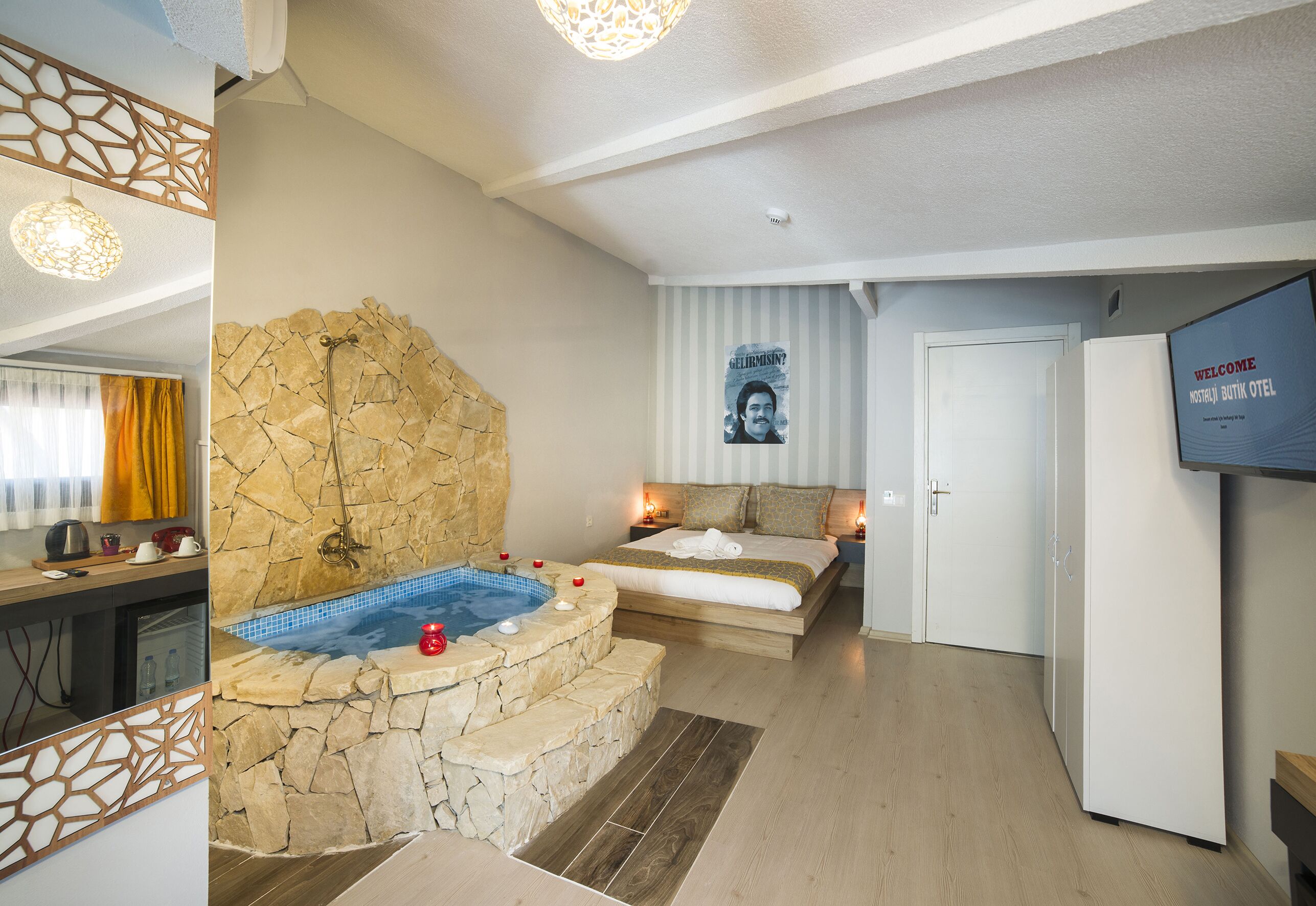 A modern hotel room with a stone wall, a hot tub, a bed with a view, and a television on the wall.