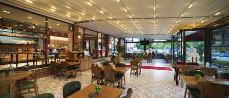 A modern cafe with wooden tables and chairs, a patterned floor, and large windows offering a view of the street outside.