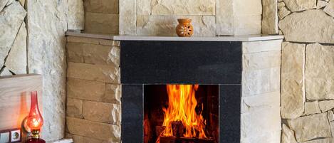 A stone fireplace with a fire burning inside, a vase on the mantel, and a candle on a table to the left.
