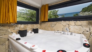A hot tub with a stone wall backdrop and a view of the sea.