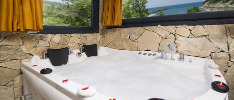 A hot tub with a stone wall backdrop and a view of the sea.