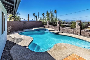 A swimming pool with a curved design, surrounded by a stone wall and a wooden fence.