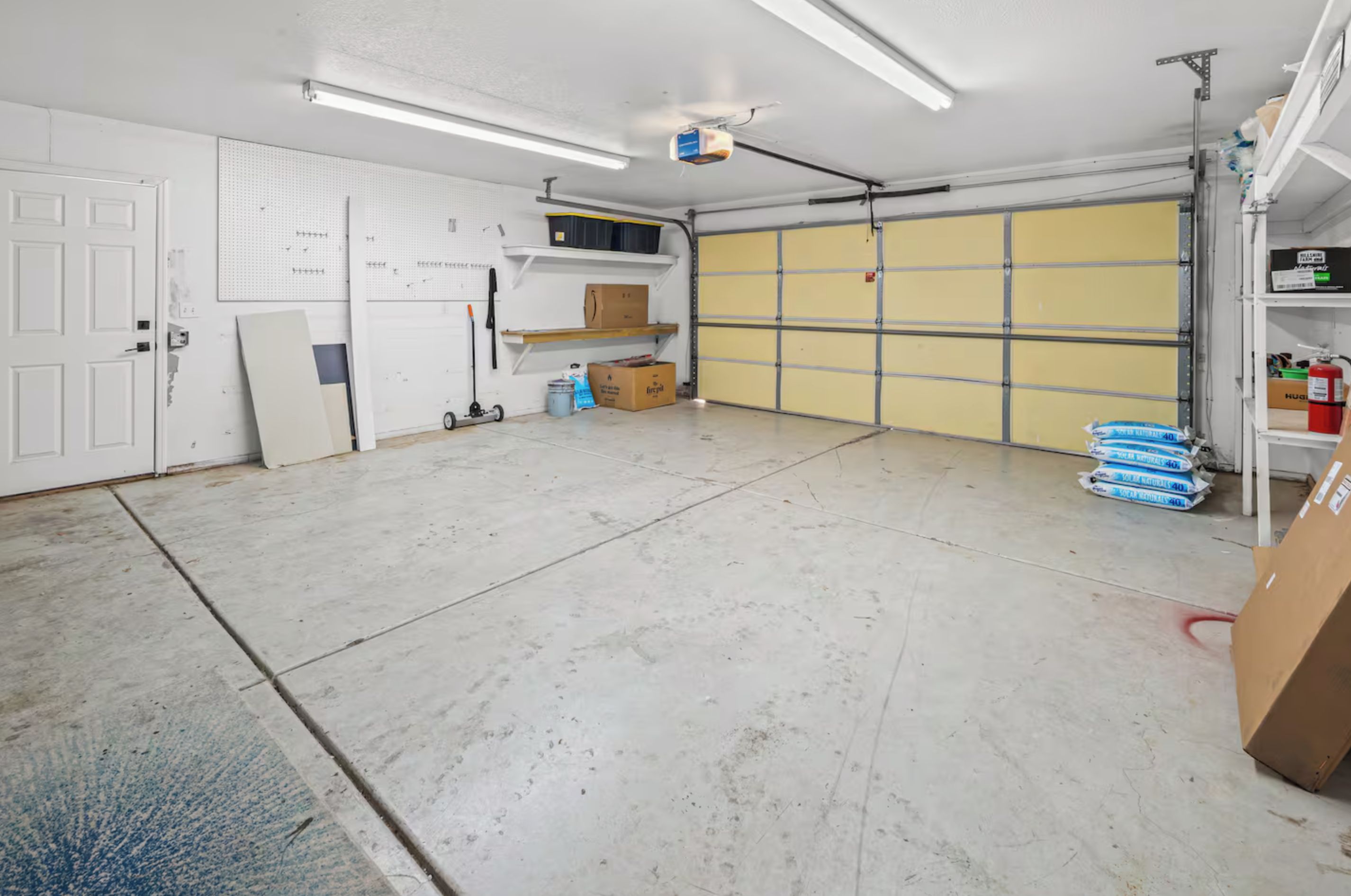 Un garage propre et bien éclairé, avec un sol en béton, une porte blanche et une porte de garage jaune.
