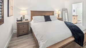 Une chambre à coucher avec un lit en bois, du linge de lit blanc, une table de chevet avec une lampe et un miroir.