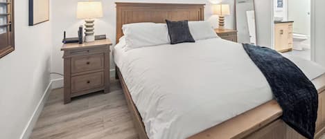 Une chambre à coucher avec un lit en bois, du linge de lit blanc, une table de chevet avec une lampe et un miroir.
