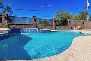Una piscina con un muro de piedra y un cielo azul despejado.