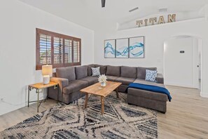 Una sala de estar moderna con un sofá seccional, una mesa de centro de madera, un tapete estampado y una ventana con persianas.