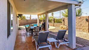 Un patio couvert avec une piscine, du mobilier d’extérieur et un mur en pierre.