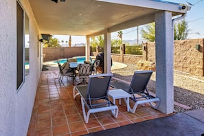 A covered patio with a pool, outdoor furniture, and a stone wall.