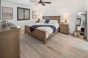 Un dormitorio con una cama de madera, mesitas de noche, un ventilador de techo y obras de arte en las paredes.