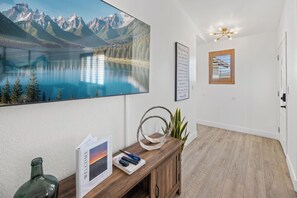 Una habitación con un cuadro de un lago montañoso, un escritorio de madera con un folleto de bienvenida, una planta y una lámpara de techo.
