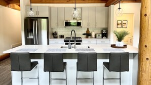 Une cuisine moderne dotée d’un îlot central, d’appareils électroménagers en acier inoxydable et de poutres en bois au plafond.