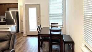 A modern kitchen with stainless steel appliances, a dining area with wooden furniture, and a view of the outside through a door. - SeaWorld & Lackland Air Force Base Modern Home (San Antonio)