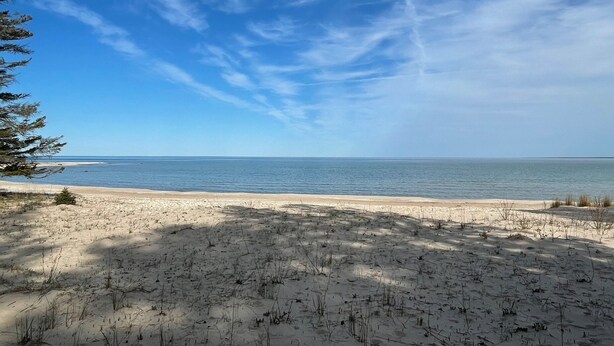 A beach with clear skies and calm water. - Island Getaway! Nestled in the woods with easy access to sandy beach (Point aux Pins)