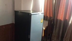 A compact kitchenette with a refrigerator, a chair, and a window with curtains. - Intouch vientiane (Vientiane)
