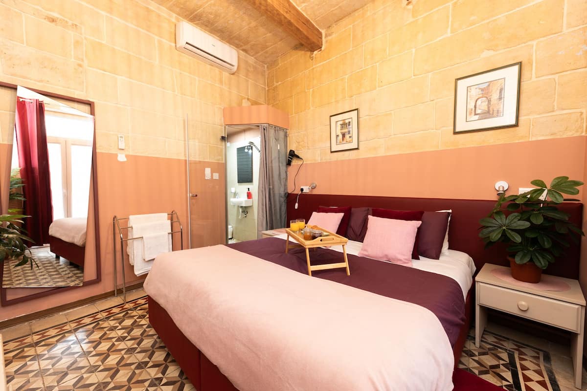 A hotel room with a bed, bedside table, and a potted plant.