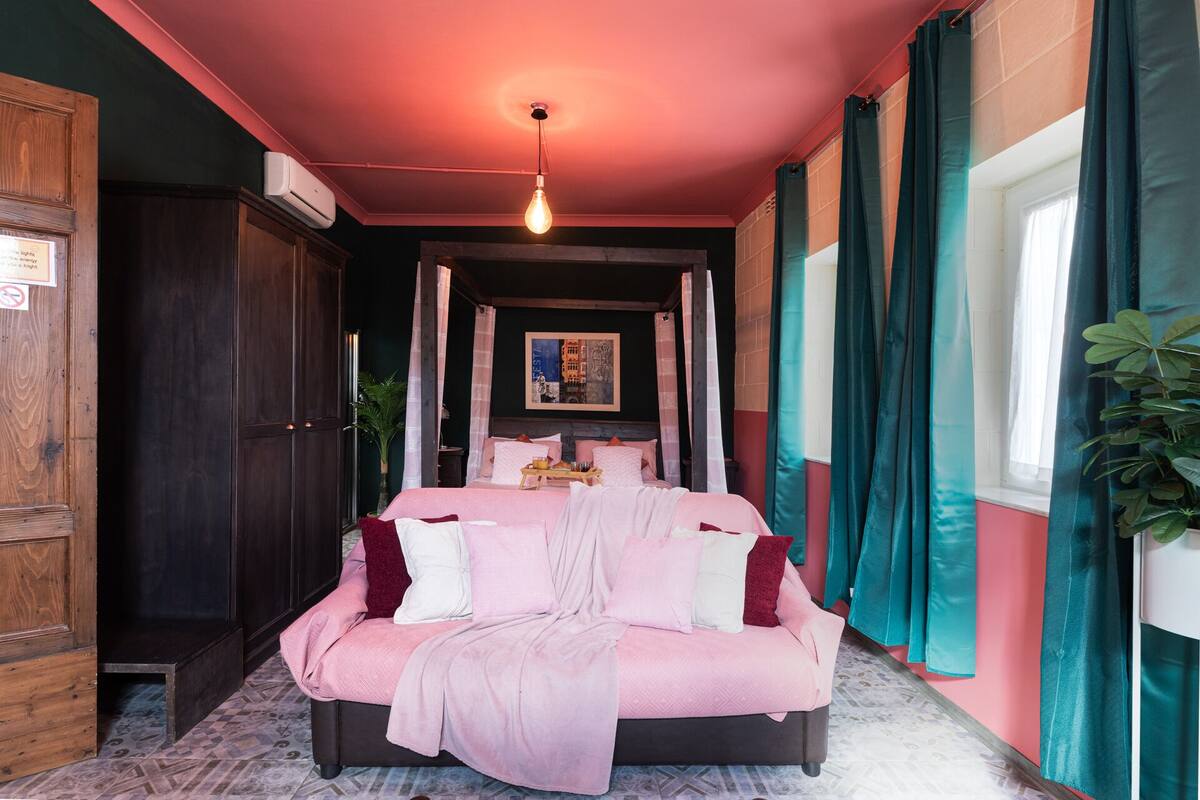 A bedroom with a large bed, a nightstand, a wall-mounted air conditioner, and a window with curtains.