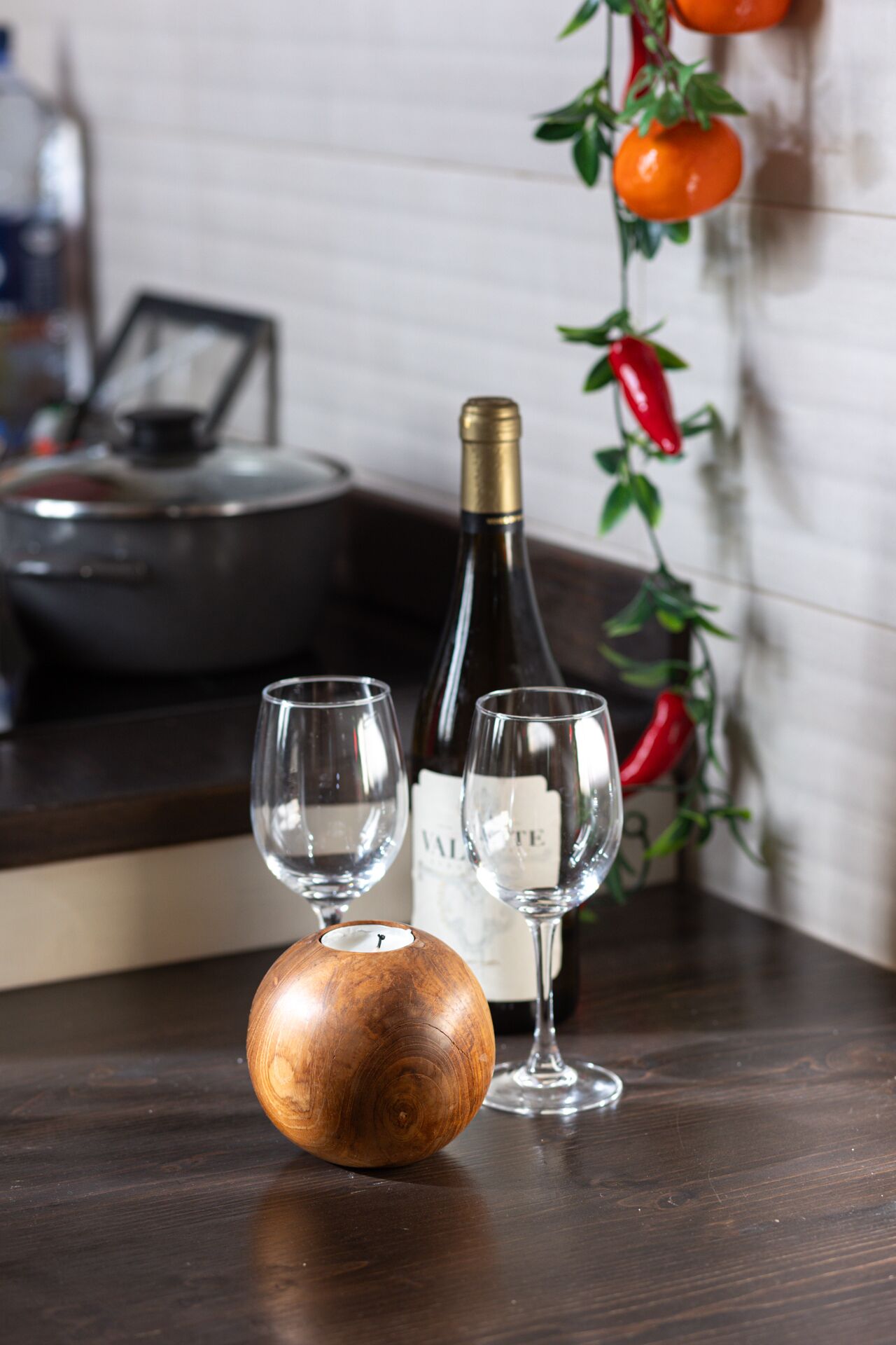 A wooden candle holder, two wine glasses, and a wine bottle on a dark wooden table.