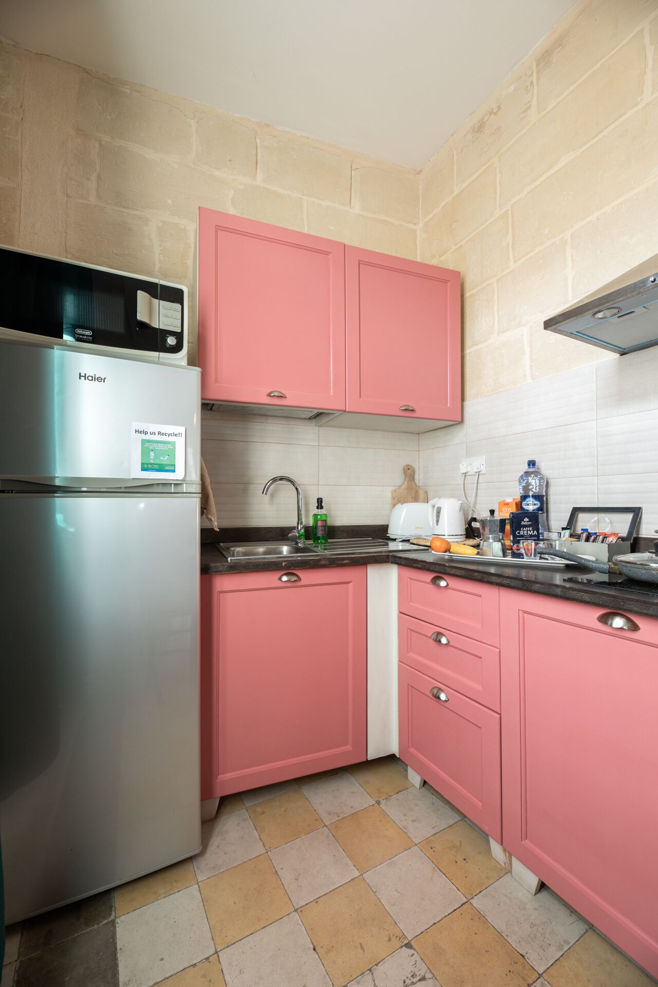 A compact kitchen with pink cabinets, a stainless steel refrigerator, and a microwave.