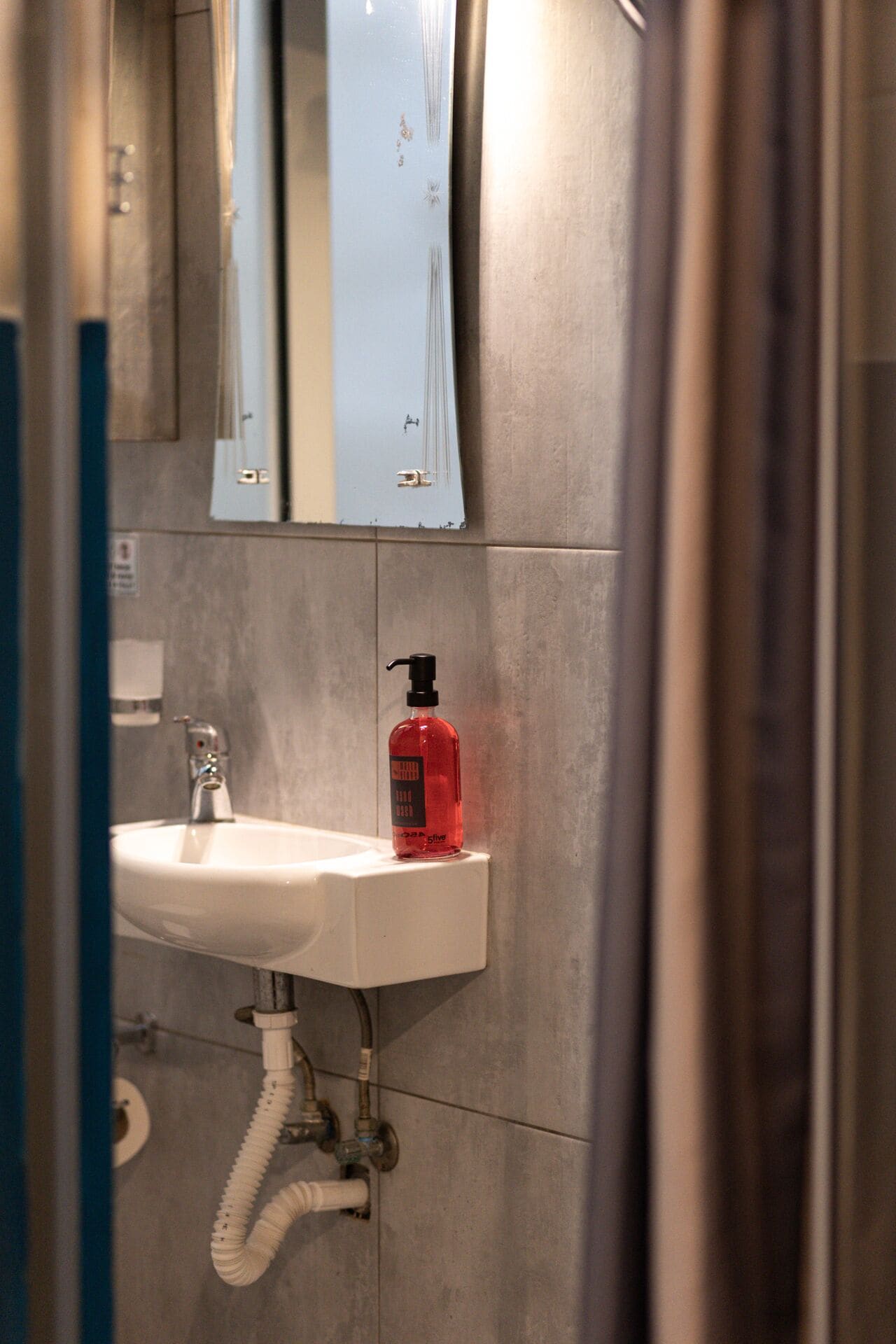 Un baño con un lavabo blanco, un dispensador de jabón rojo y un espejo sobre el lavabo.