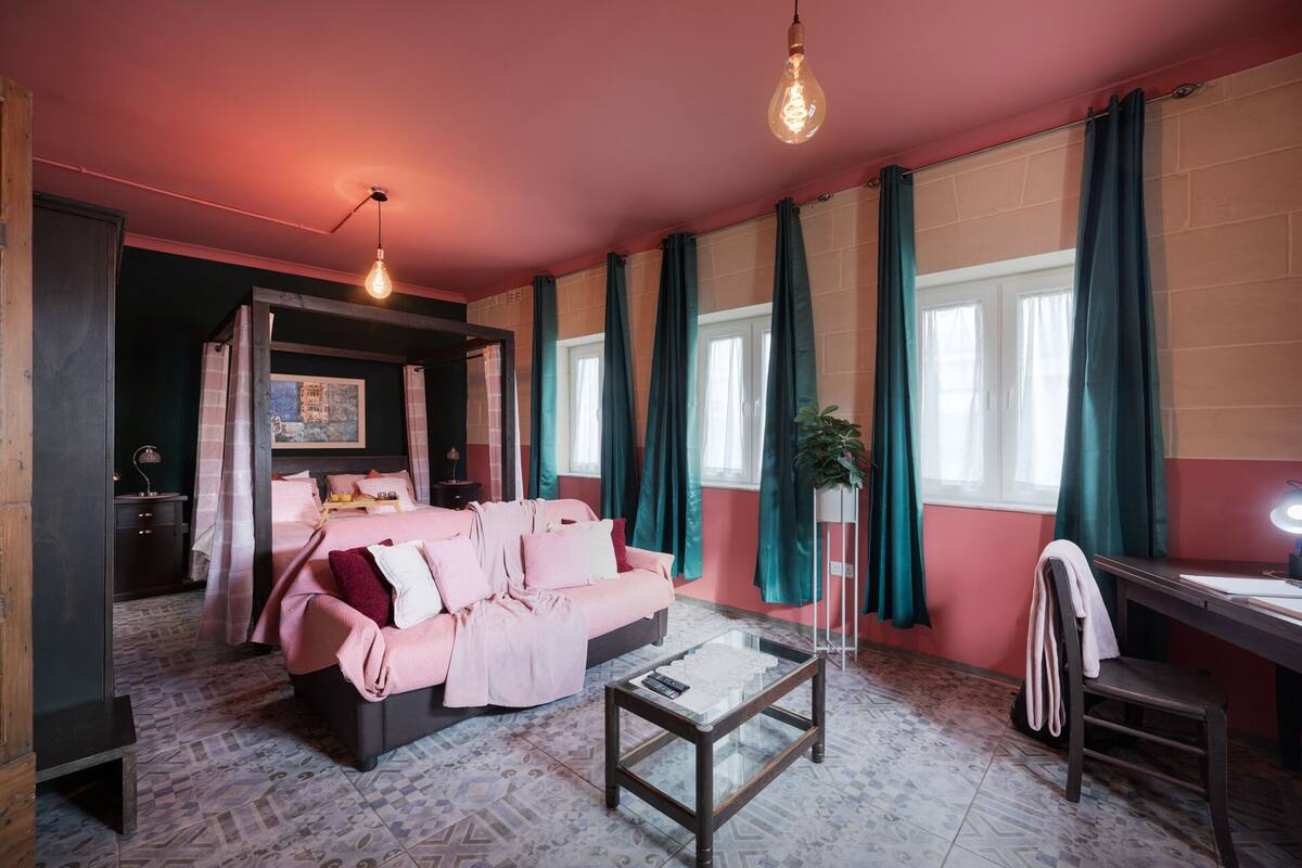 A room with a bed, a coffee table, a desk, and a large window with curtains.