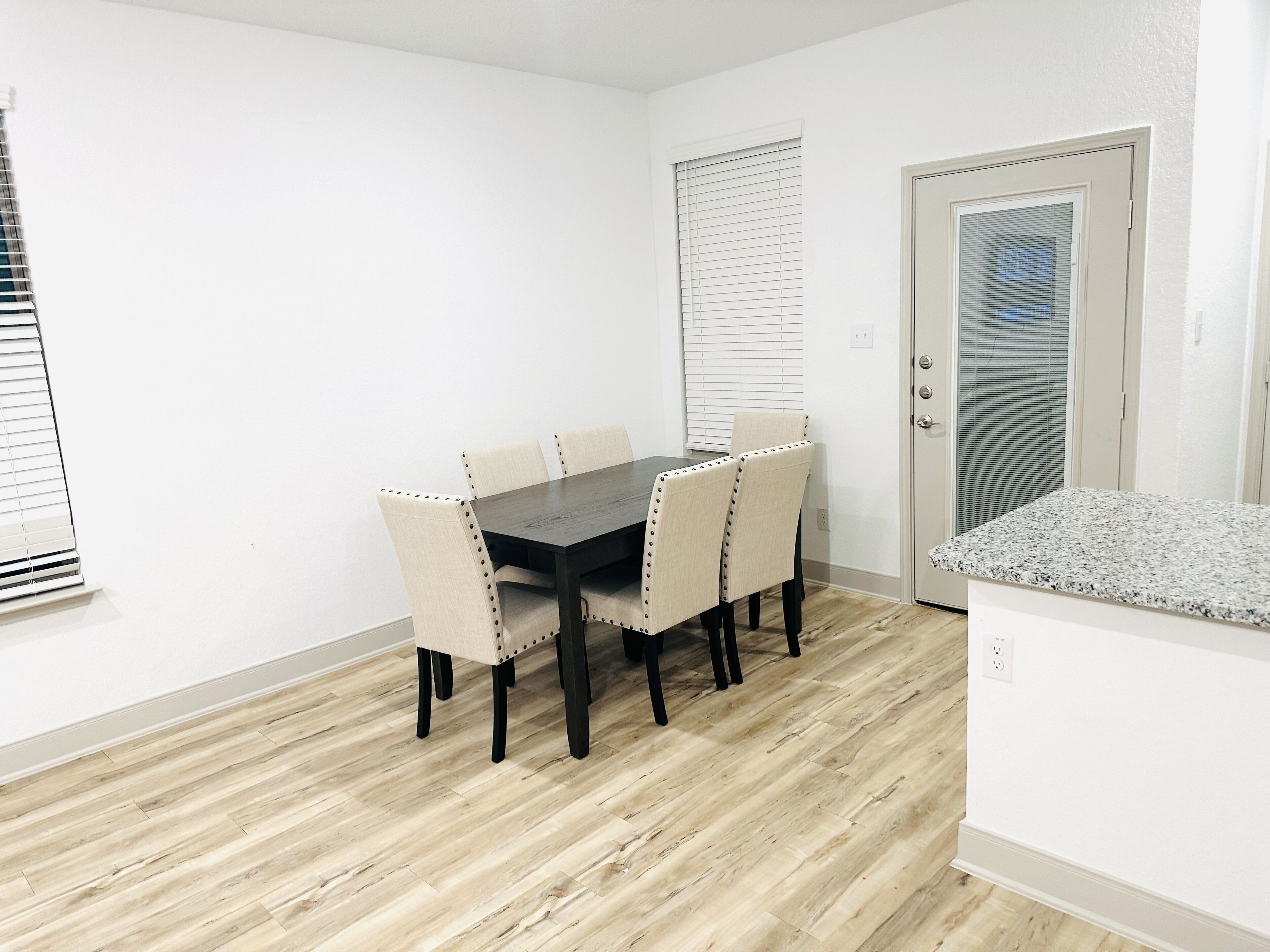 A dining area with a wooden table and six chairs, a door with a frosted glass panel, and a white wall.