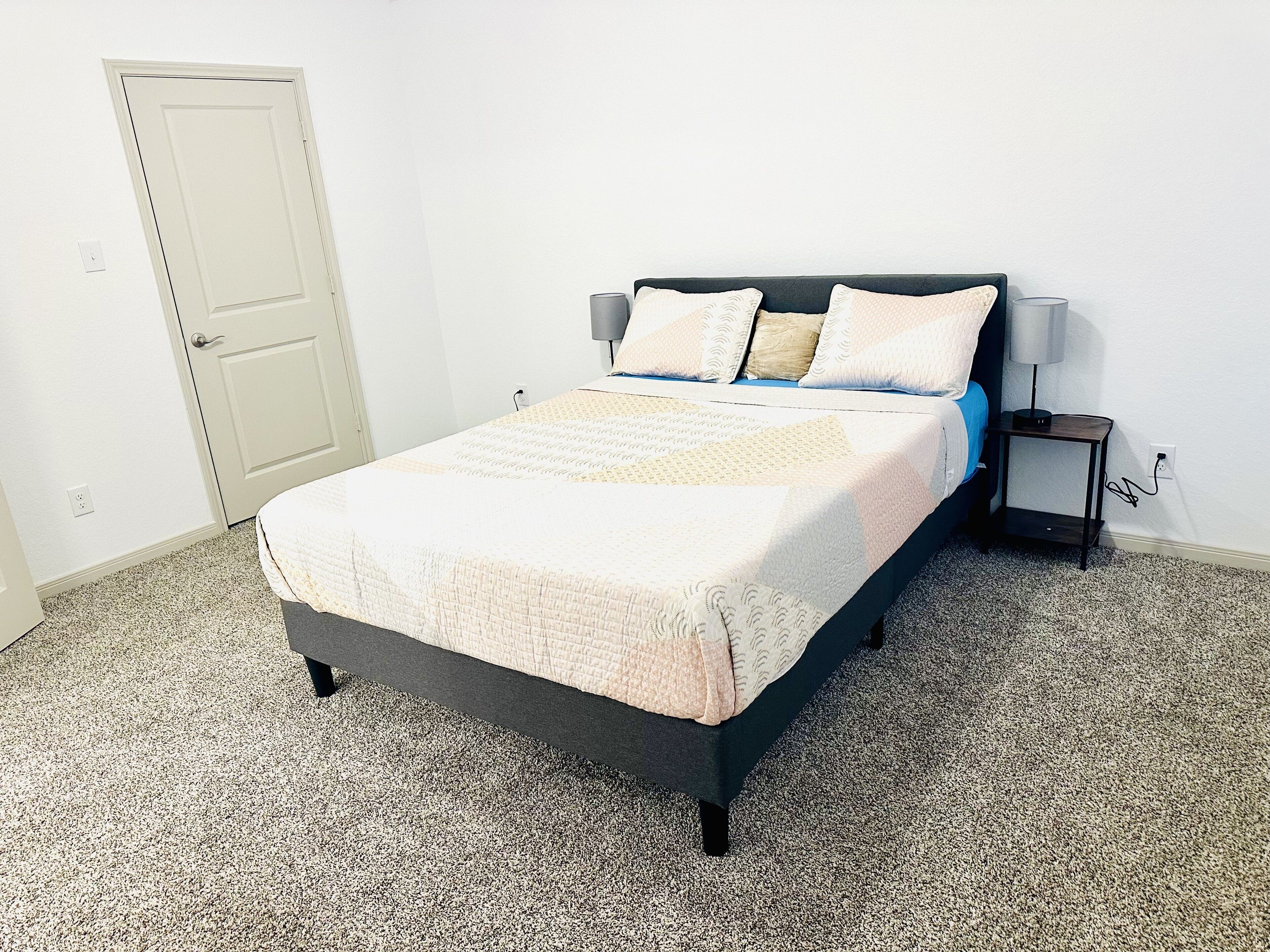 Un dormitorio con cama, mesita de noche, lámpara y puerta.