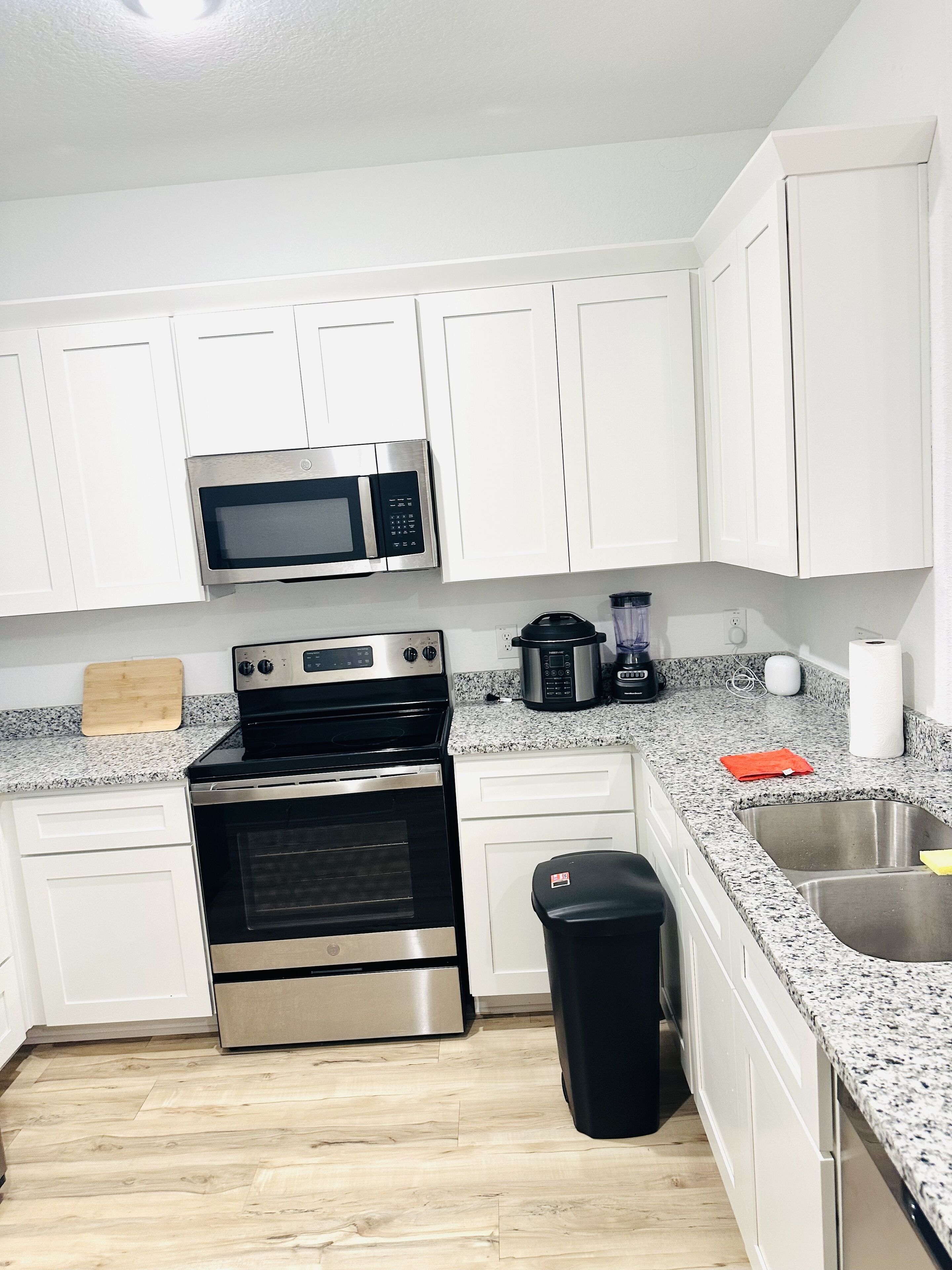 Una cocina moderna con armarios blancos, electrodomésticos de acero inoxidable, encimeras de granito y suelo de madera.