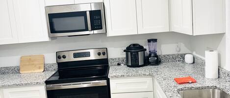 Una cocina moderna con armarios blancos, electrodomésticos de acero inoxidable, encimeras de granito y suelo de madera.