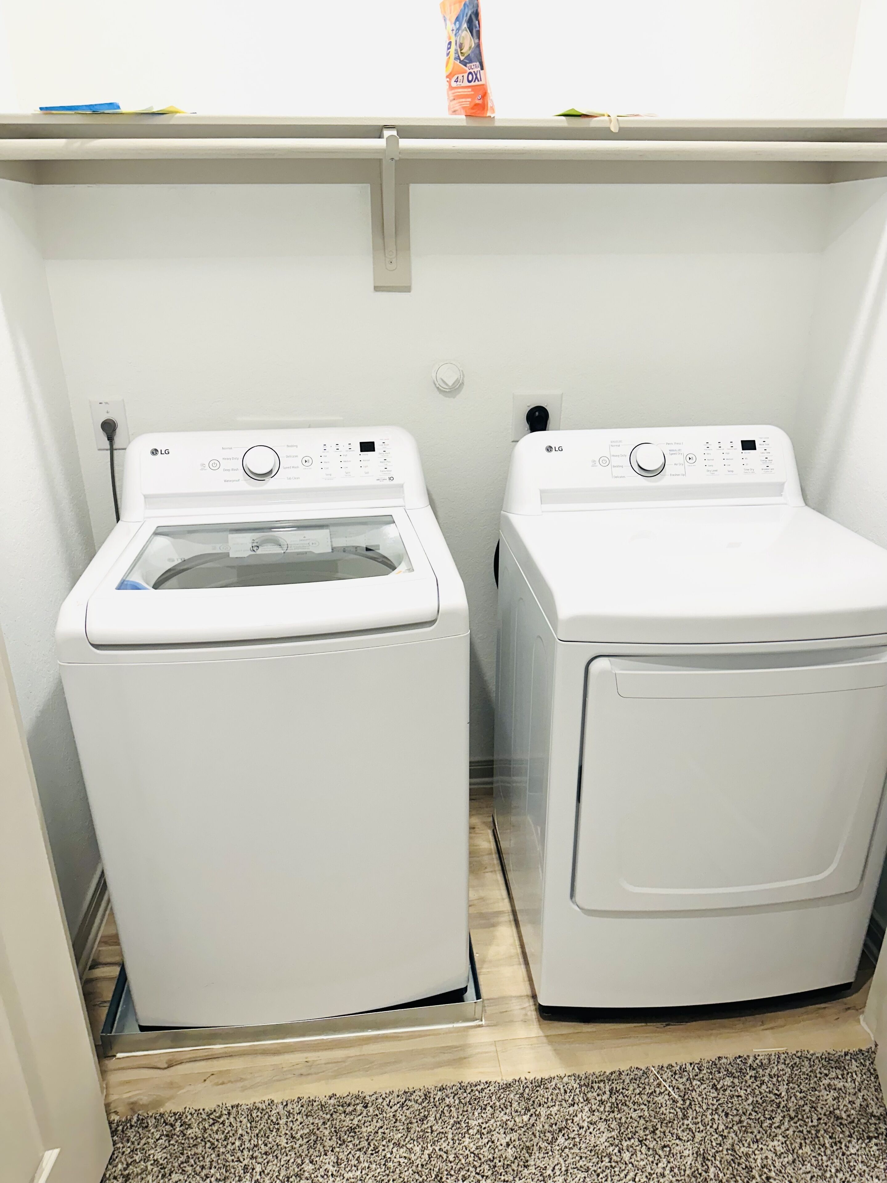 Une buanderie équipée de deux machines à laver LG à chargement frontal, de couleur blanche, avec un plancher en bois et un mur blanc.