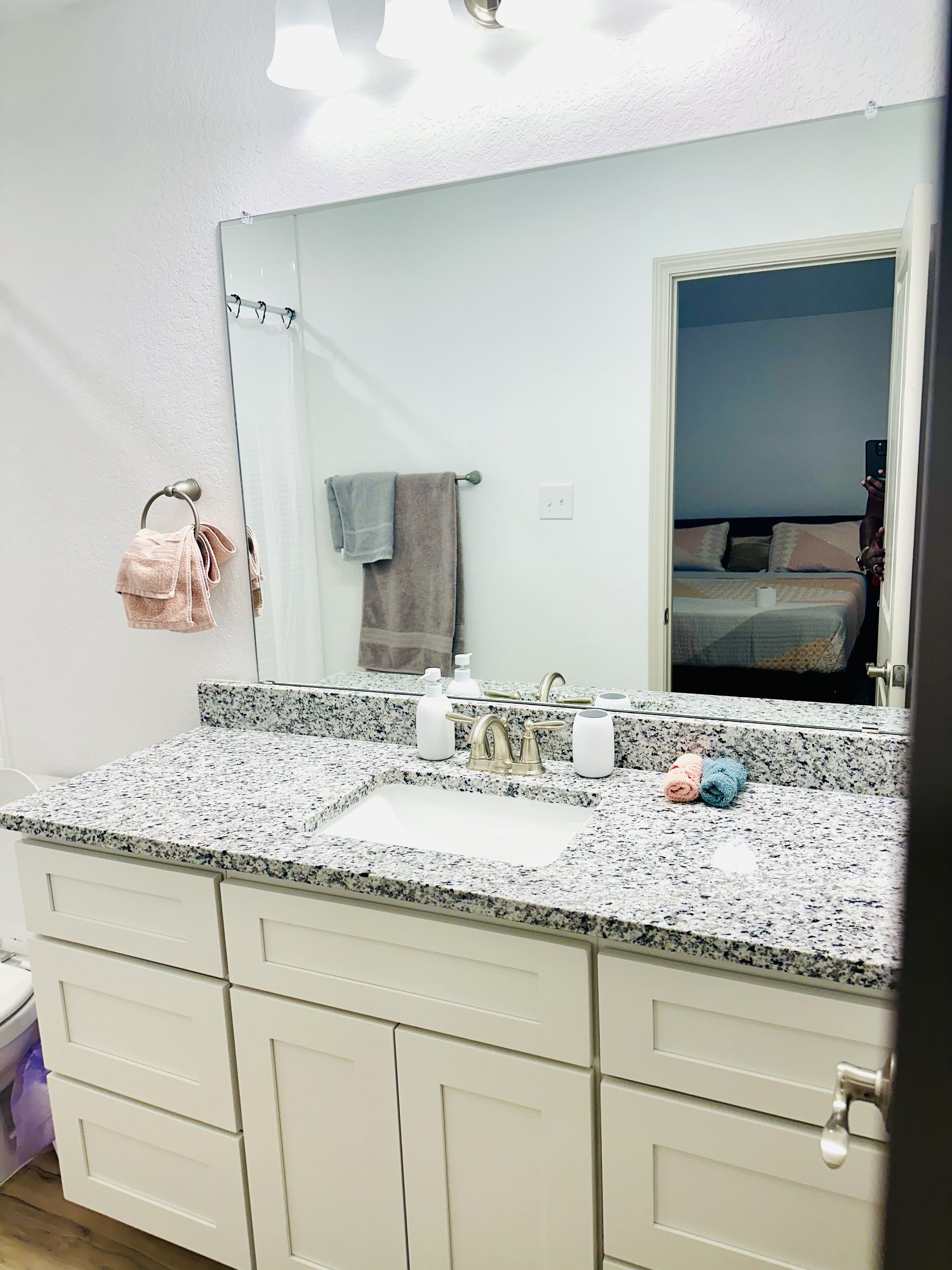 A bathroom with a granite countertop, a sink, a mirror, and a towel rack.