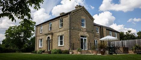 A two-story brick house with a front door, windows, and a patio area with outdoor furniture.